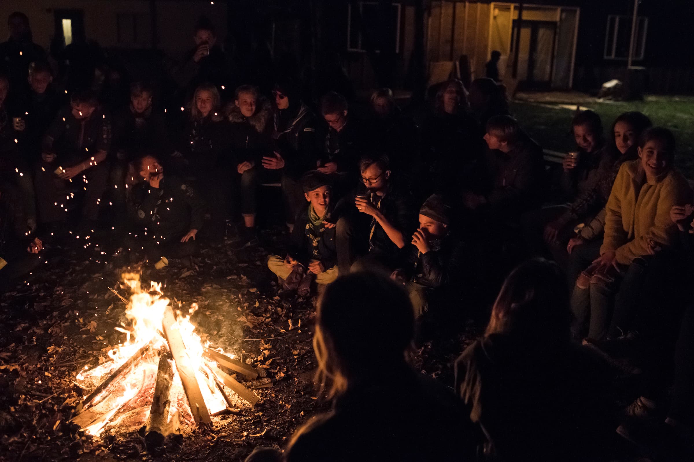 En stor grupp scouter som sitter kring en lägereld