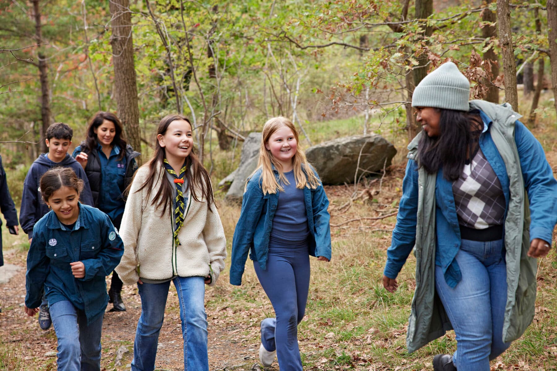 En grupp människor går tillsammans i en skogsmiljö, med träd och stenar i bakgrunden.
